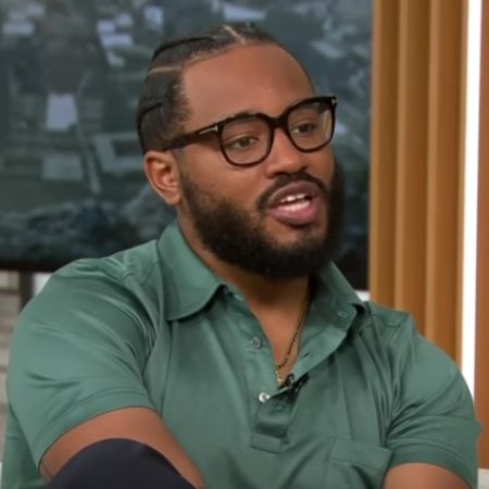 Ryan Coogler is wearing a grey polo shirt and glasses.